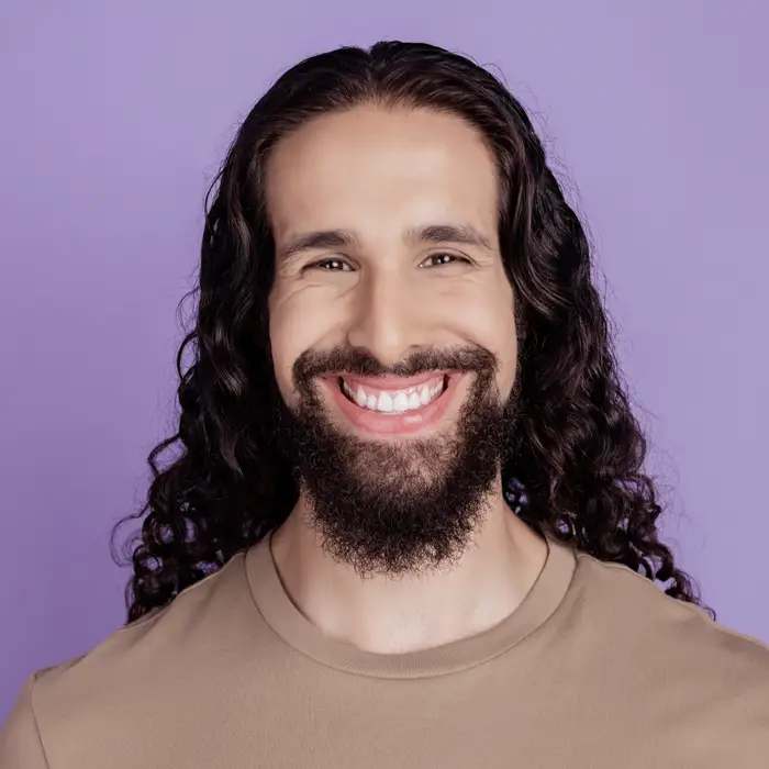 A young man in front of a purple backgrounding smiling brightly