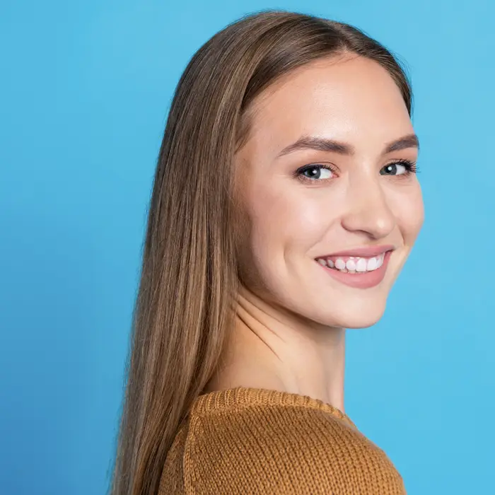 A young woman in front of a blue background smiling