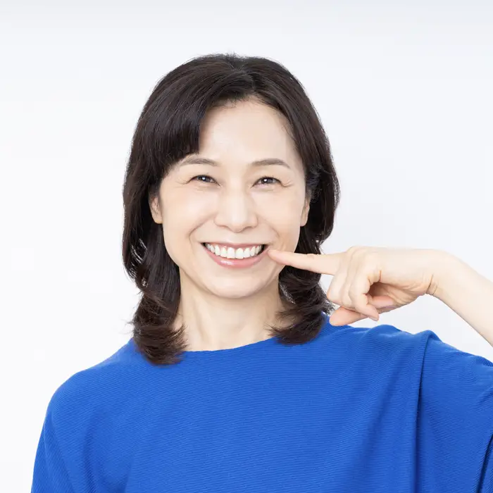 A middle aged woman wearing a blue shirt smiling brightly and pointing to her teeth